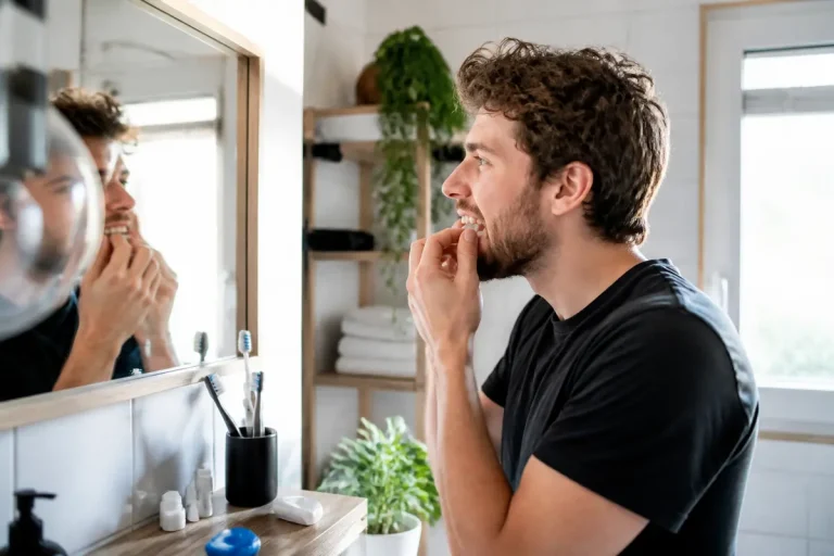 Homme devant un miroir utilisant du fil dentaire pour aligner ses dents proprement