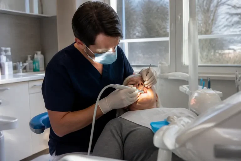 Dentiste effectuant un détartrage dentaire ultrason sur patient(e) dans son cabinet lumineux
