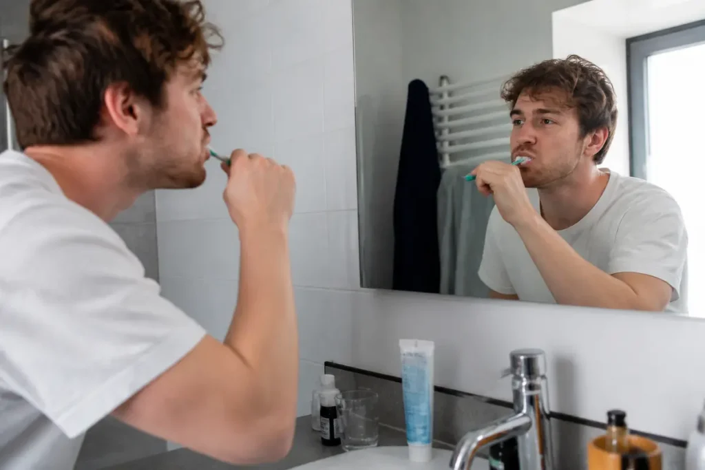 Homme se brossant les dents devant un miroir pour maintenir une bonne hygiène bucco-dentaire