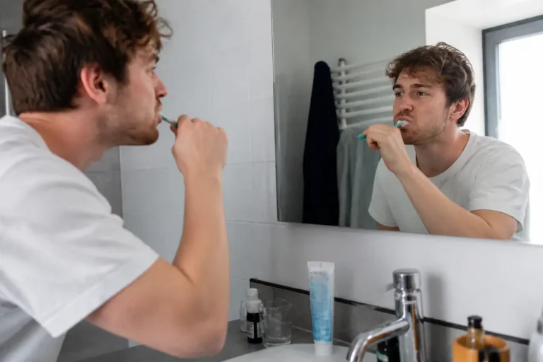 Homme se brossant les dents devant un miroir pour maintenir une bonne hygiène bucco-dentaire